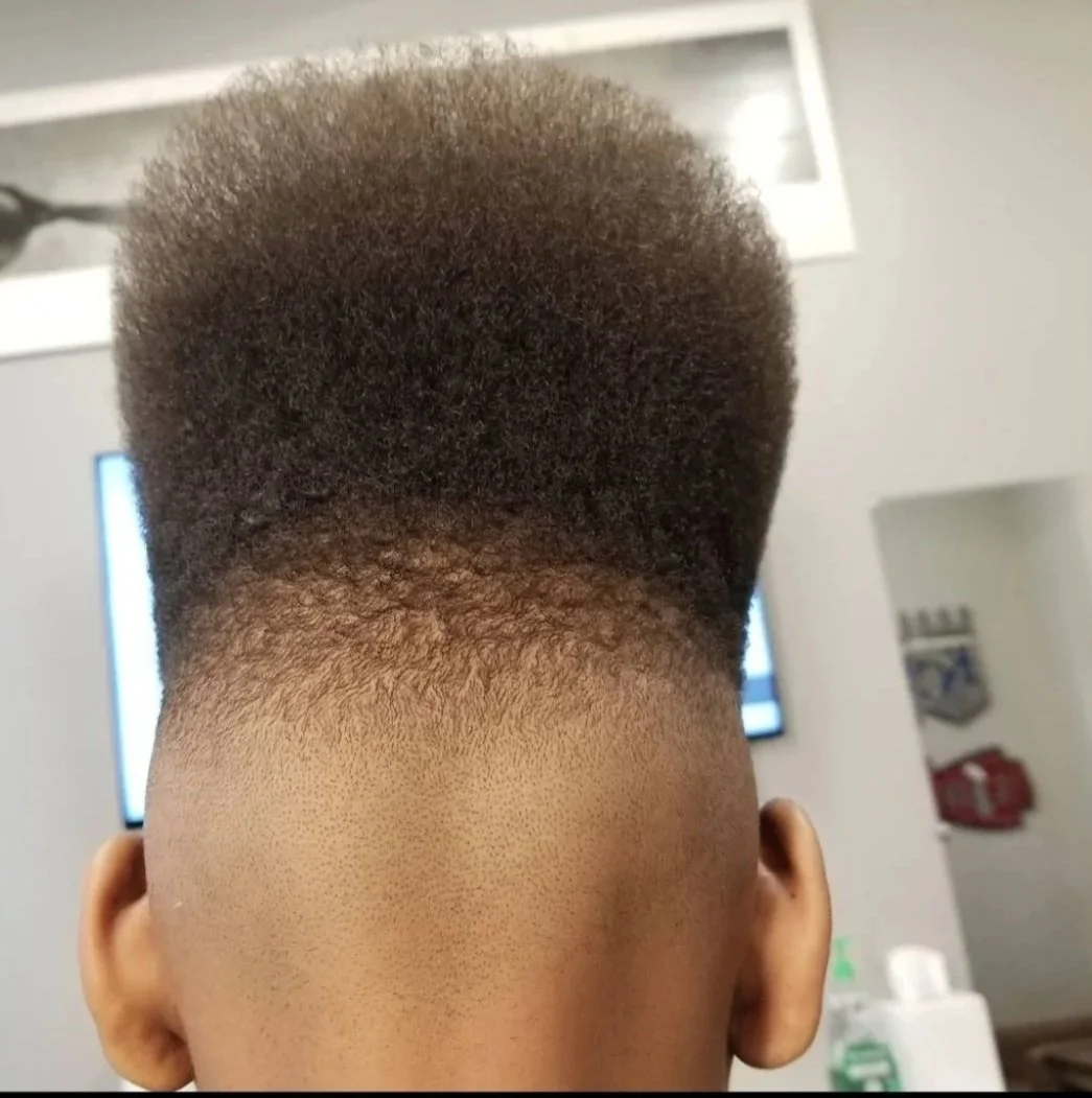 Back of a person's head with a high fade haircut, showing textured afro hair on top and skin fade on the sides, in a barbershop or salon setting.