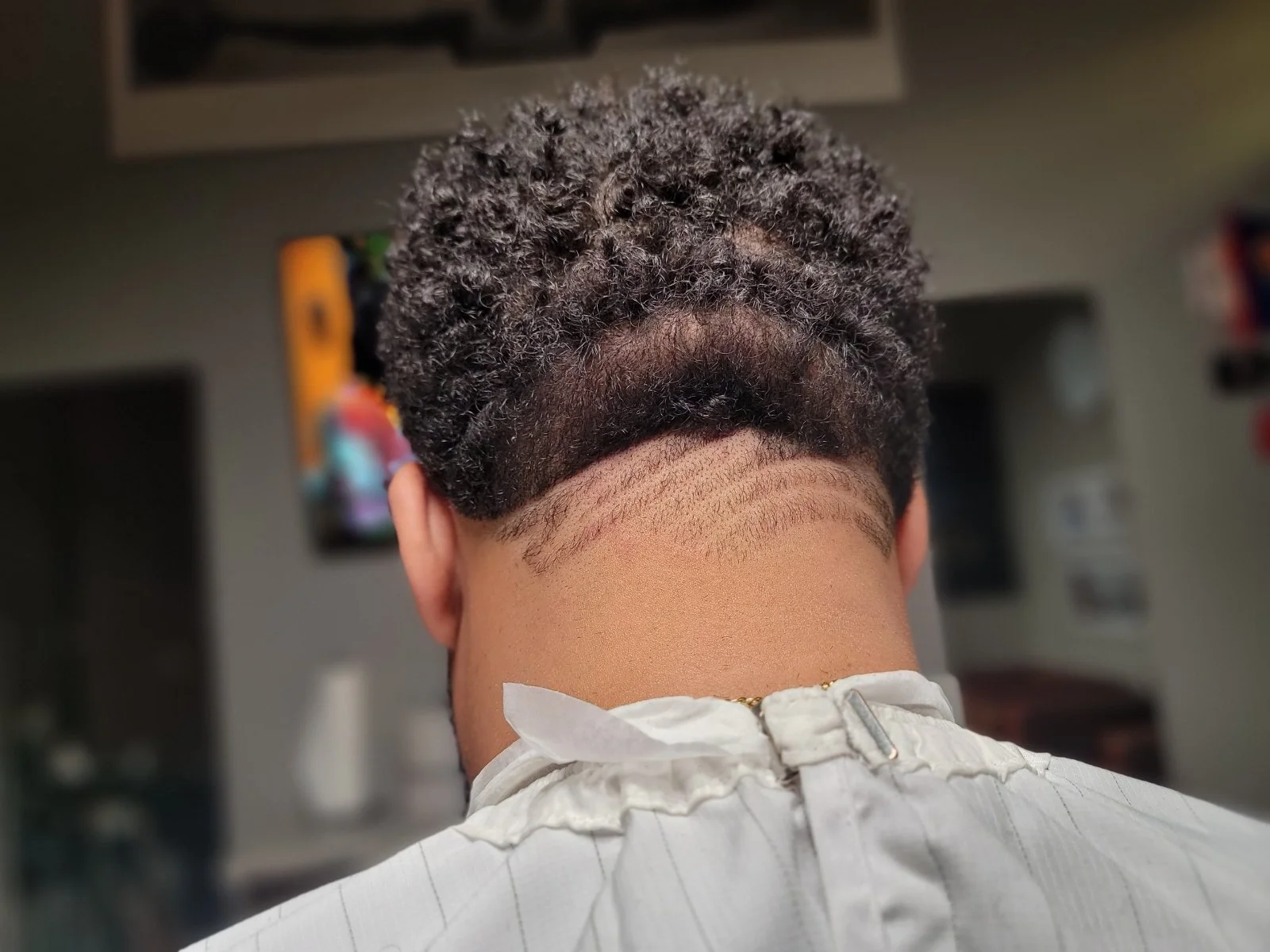 Back of a person's head showing a fresh haircut with textured curly hair and a fade, wearing a white shirt