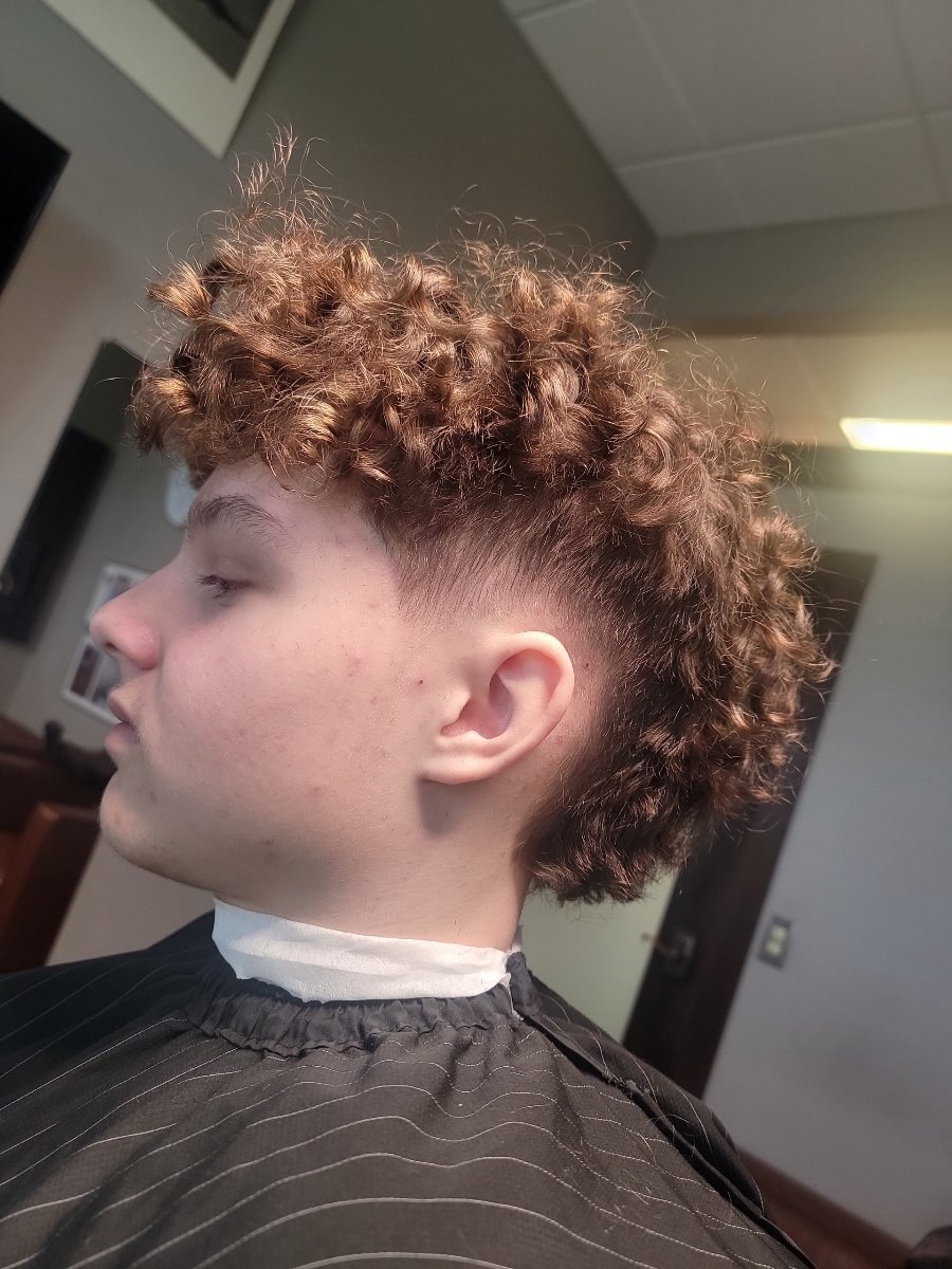 A person with curly brown hair getting a fade haircut at a barber shop.