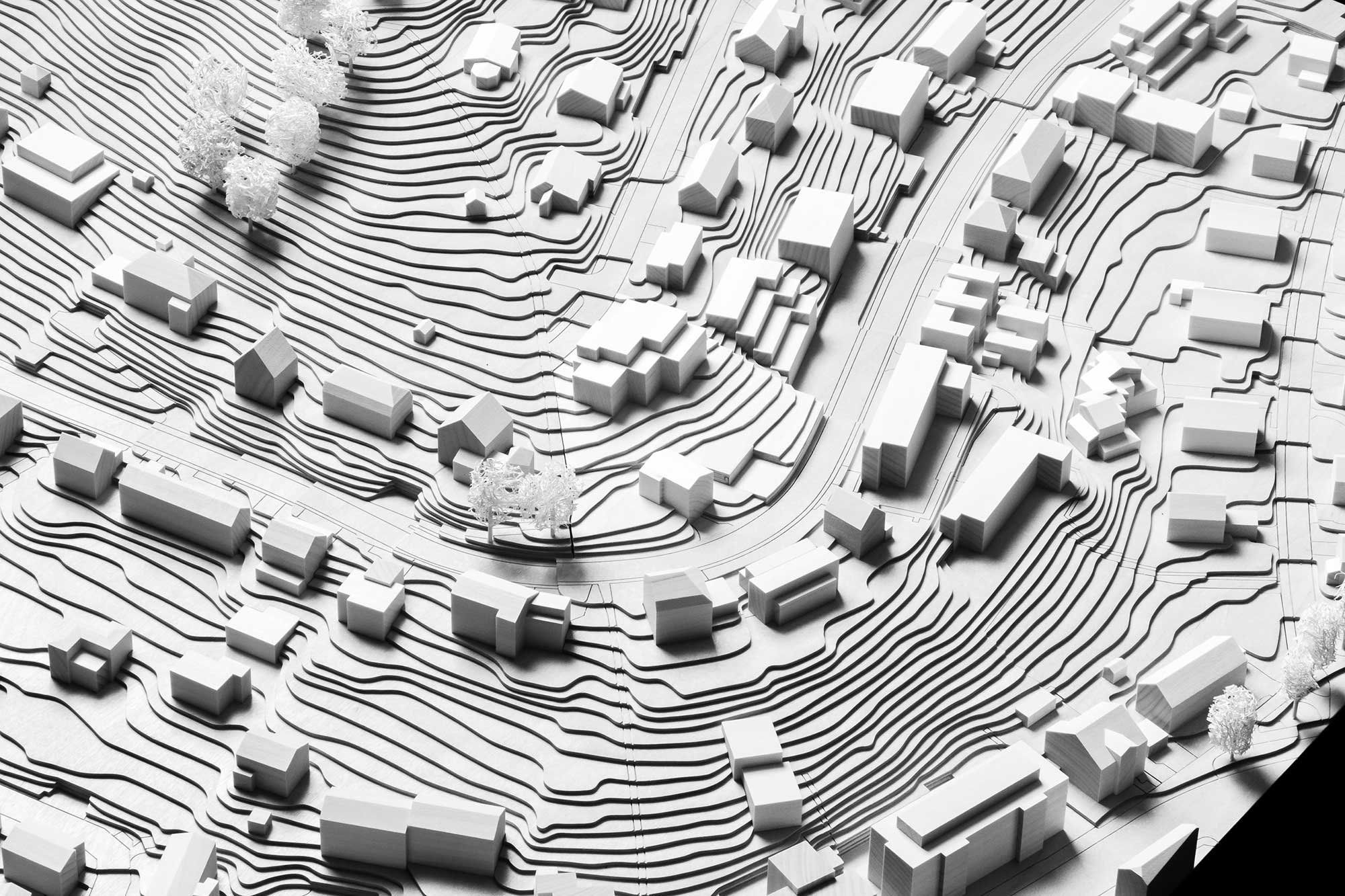Architekturmodell eines Hügellands mit verschiedenen Gebäuden, Straßen und Bäumen.