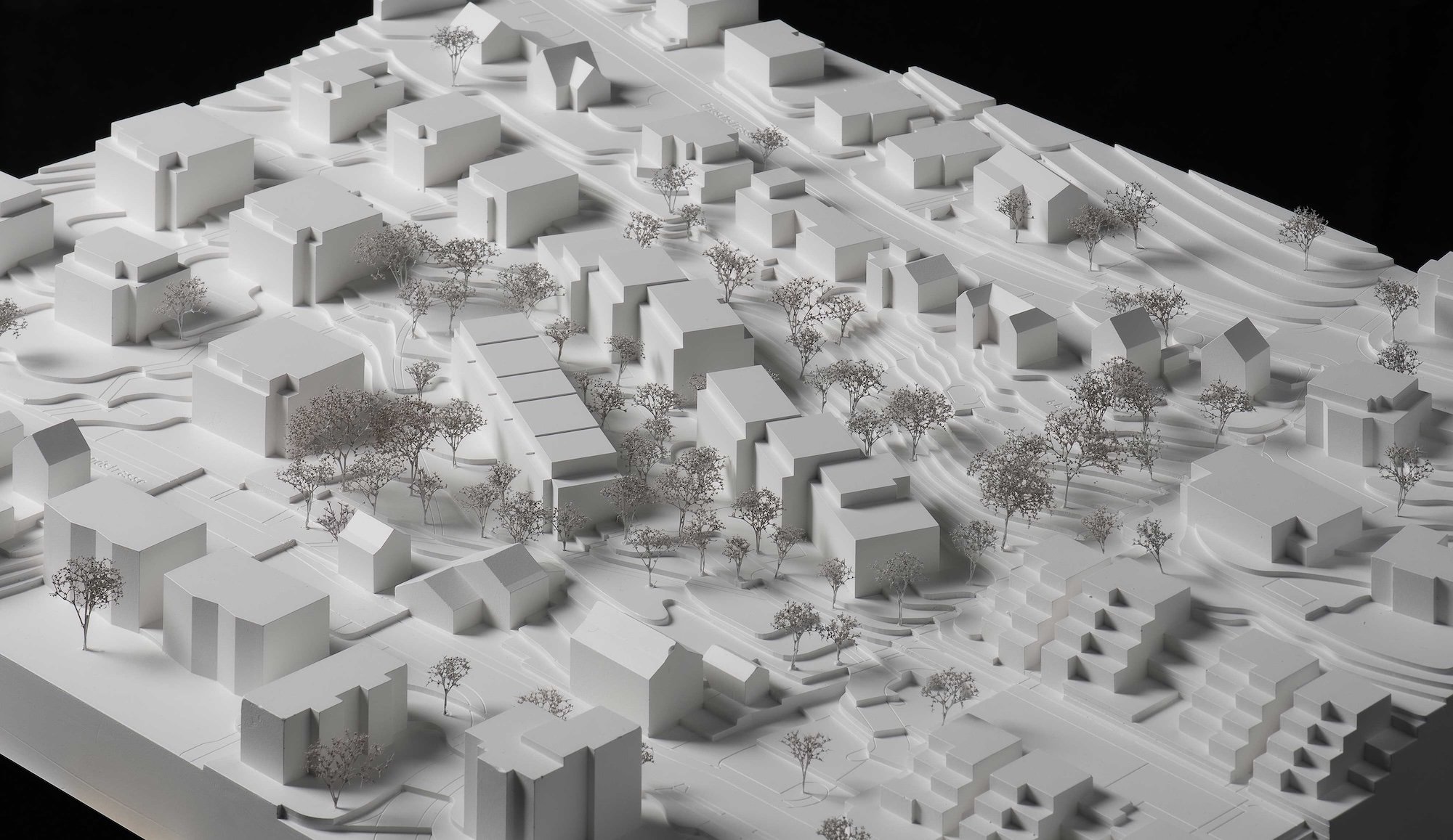 Ein Weißmodell eines Stadtteils mit Gebäuden, Straßen und Bäumen auf einem schwarzen Hintergrund.