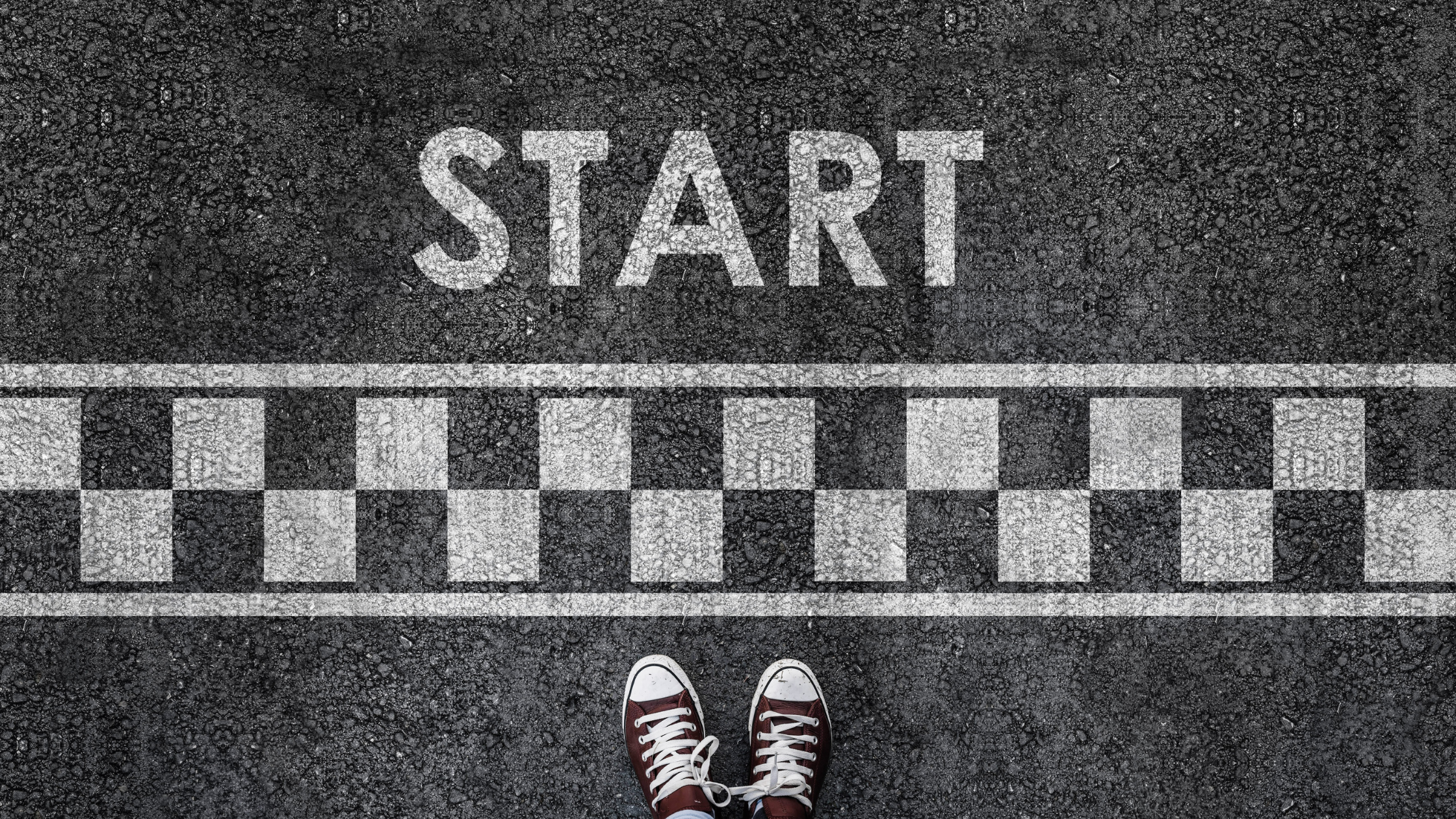 A pair of sneakers at a starting line on a checkered road with the word 'START' painted, symbolizing the challenge of beginning tasks and building momentum.