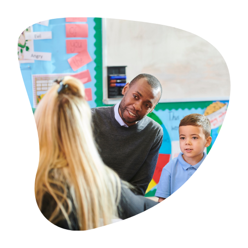 A teacher engages warmly with a parent and his child in a colorful classroom, representing supportive school relationships after ADHD disclosure.
