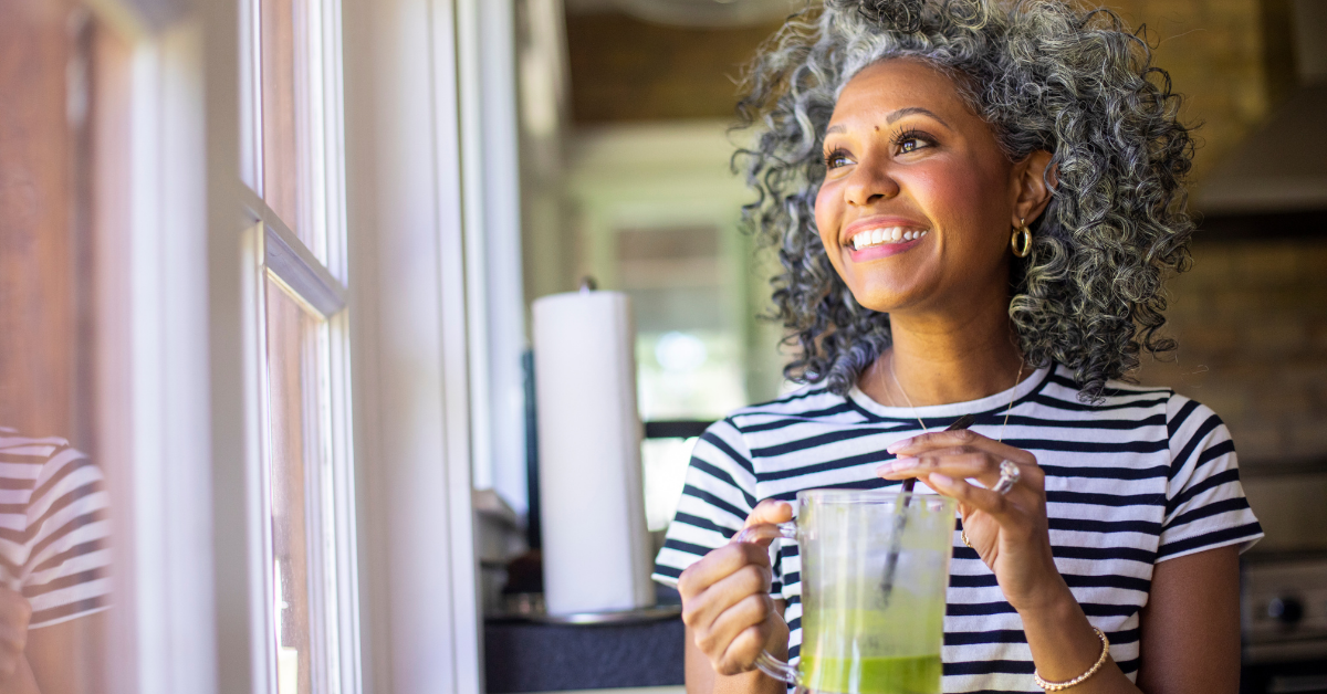 Woman smiling and holding a green smoothie, enjoying a calm morning routine