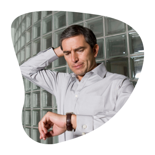 A man in a light gray shirt, looking concerned while checking the time on his watch, symbolizing the stress of running late or poor time management.