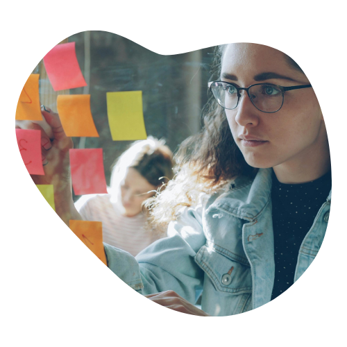 A focused woman wearing glasses placing colorful sticky notes on a transparent surface, symbolizing externalized structure and organization for managing tasks effectively.