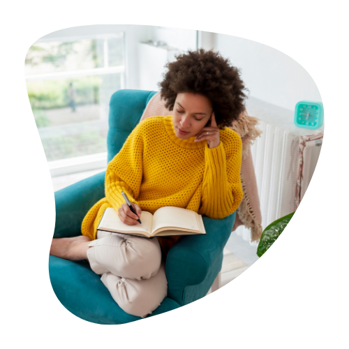 A woman in a yellow sweater sitting in a cozy chair, writing in a notebook, portraying the process of creating a personalized dopamine menu to stay motivated.