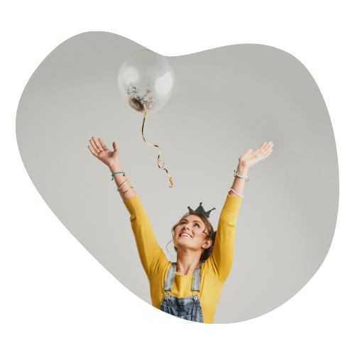 A smiling woman in a yellow shirt tosses a balloon into the air, expressing joy and letting go of limiting beliefs.
