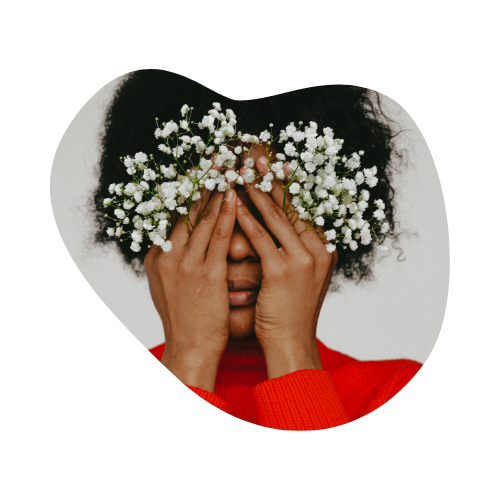 A woman in a red sweater holding small white flowers in front of her face, symbolizing self-expression, growth, and blooming into one's identity.