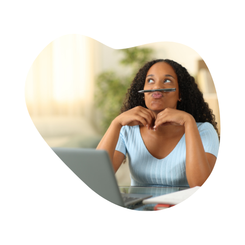 A young woman sitting in front of a laptop, playfully balancing a pen on her upper lip while gazing upward — a relatable moment of distraction and daydreaming.