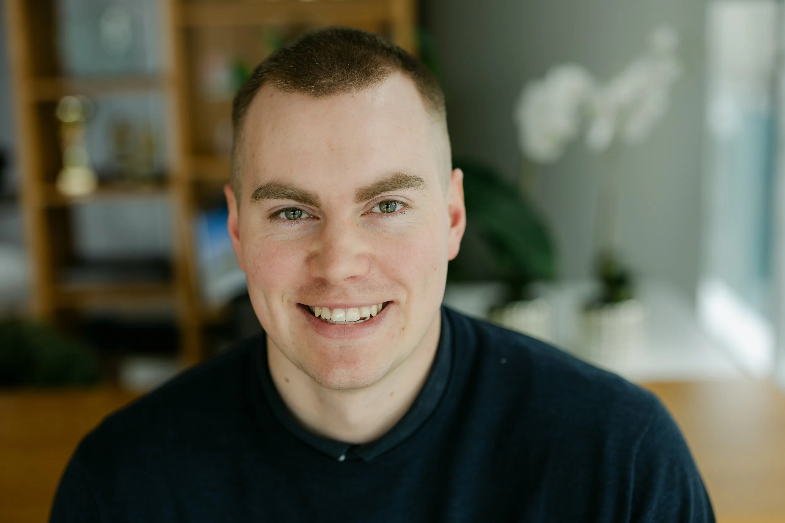 A smiling young man with short brown hair and blue eyes in an indoor setting.
