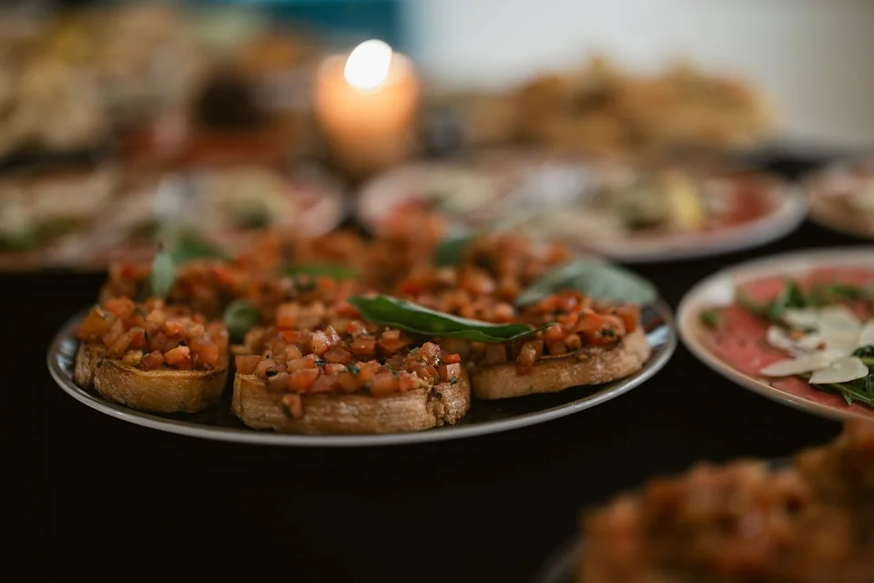 Plate of bruschetta topped with diced tomatoes and basil, with other dishes blurred in the background.