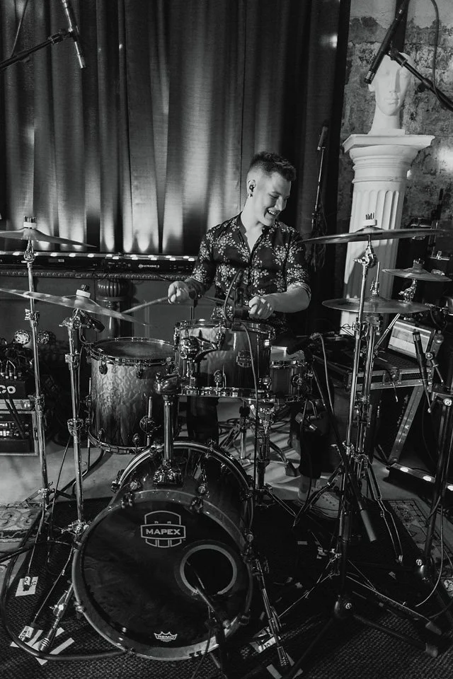 A person playing a drum set in a recording studio with microphones and music equipment.