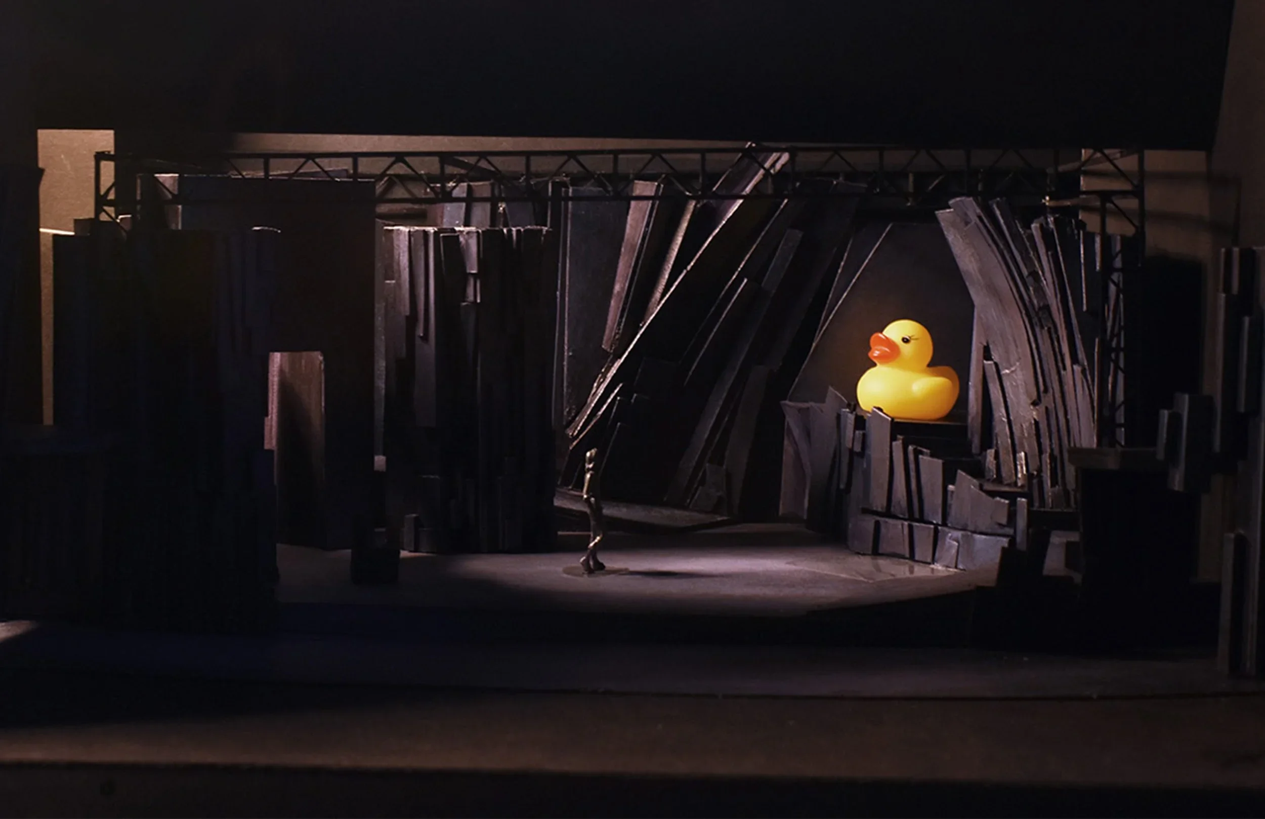 A lone figure regards a giant rubber ducky in a twisted black landscape.