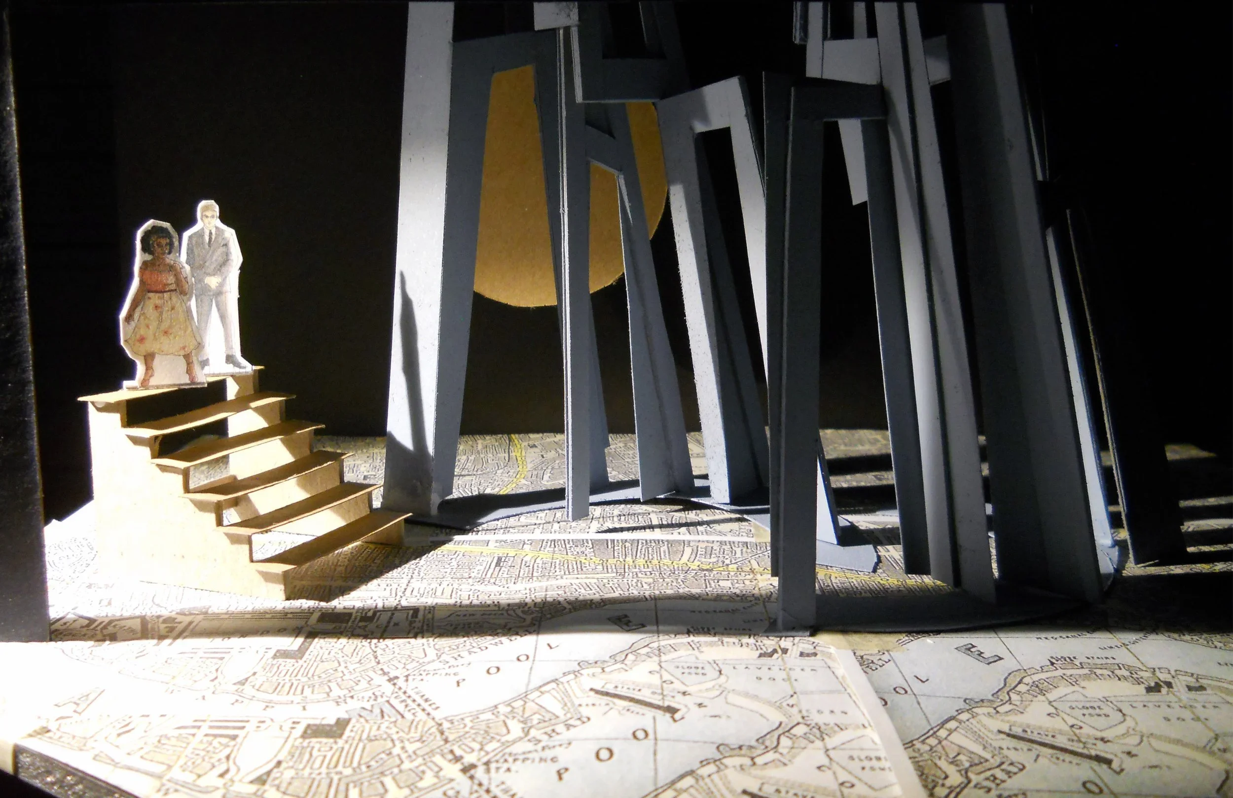 A male-presenting figure stands behind a female-presenting figure atop a short staircase. To their right is a forest of grey archways, backed by a giant moon. The floor describes a map.