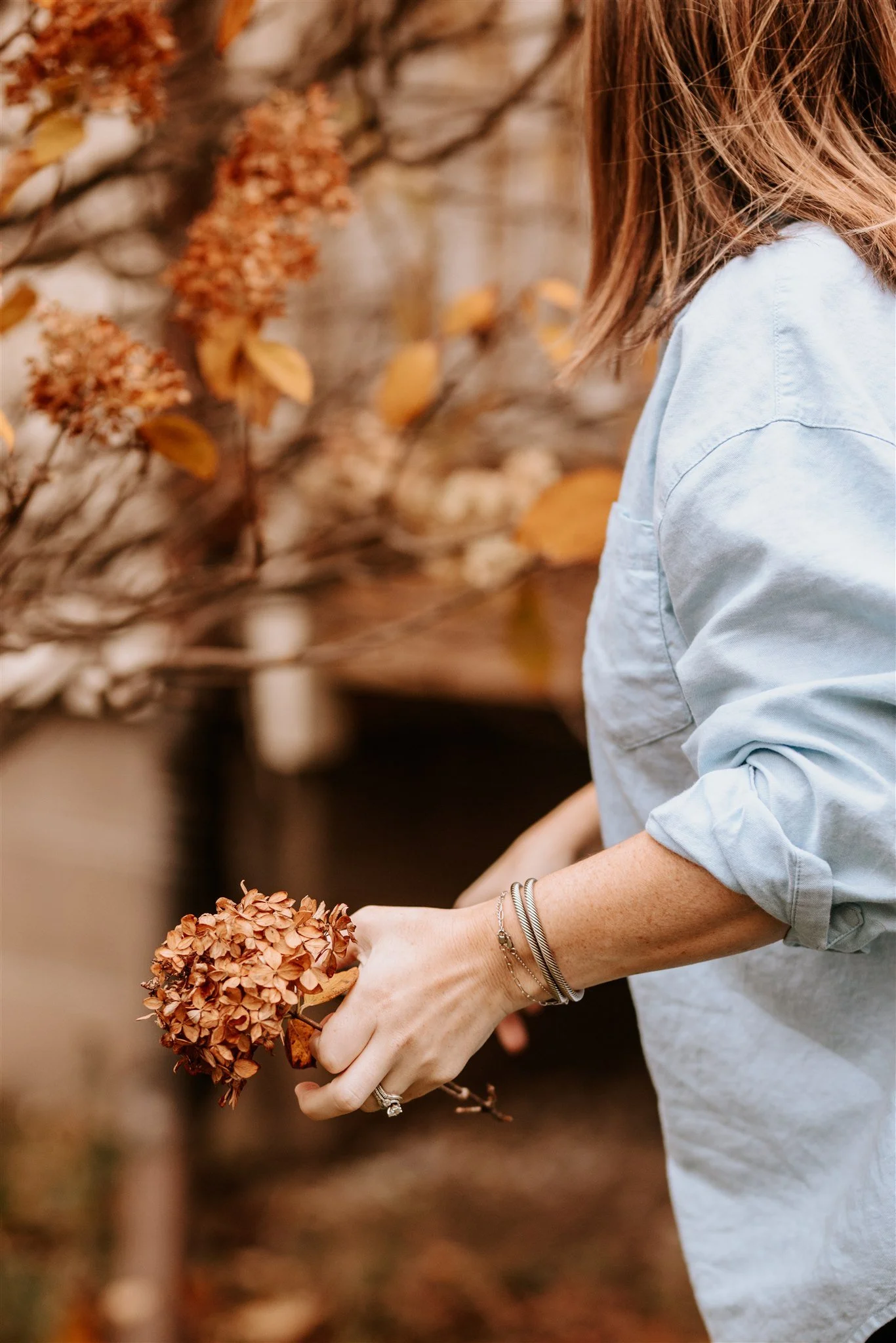 A person with light brown hair wearing a light blue shirt holding a dried flower bouquet in their right hand.