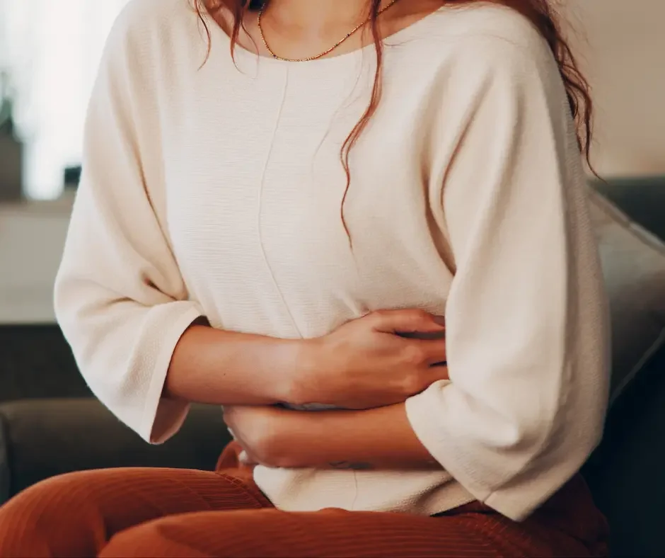 Woman experiencing abdominal discomfort and holding her lower abdomen, representing menstrual and PMS symptoms.