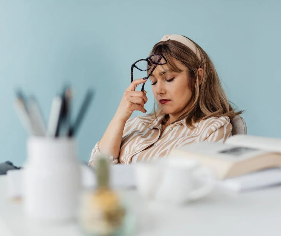 Woman sitting at a desk with her eyes closed, experiencing fatigue and low energy, representing chronic fatigue care at True Health Integrative Clinic in Winnipeg.