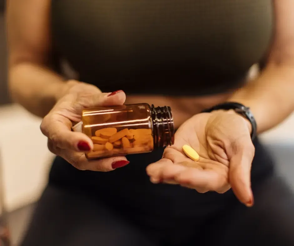 Woman holding a bottle of dietary supplements and a tablet in her hand, representing nutritional support as part of PMS care.