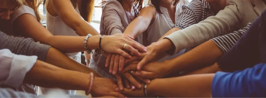 Healthcare team members placing their hands together to represent collaboration, integrated care, and a multidisciplinary approach to supporting patients with complex and chronic health concerns.