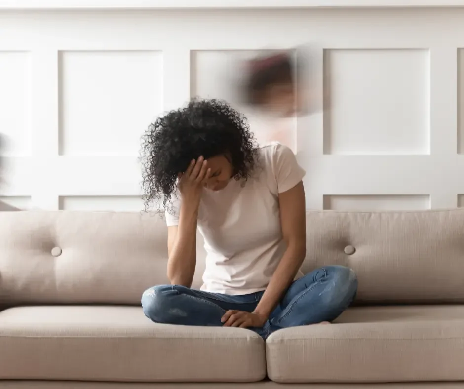 Woman sitting on a couch with her head in her hand, representing emotional overwhelm, stress, and mood changes associated with PMDD.