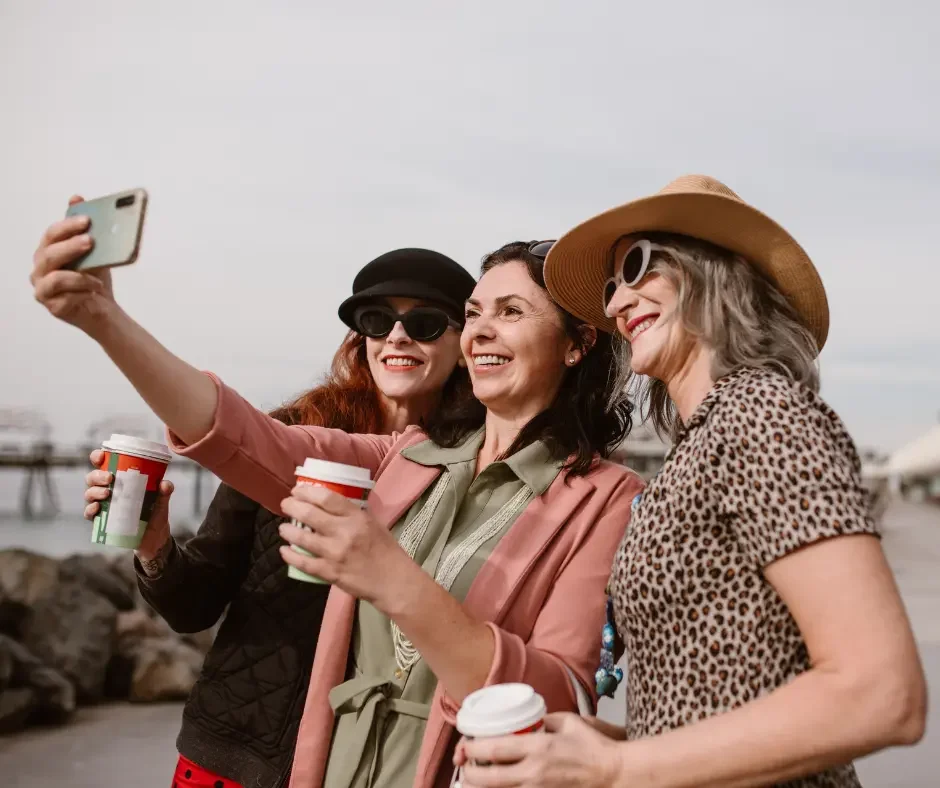 Three women smiling together while taking a selfie outdoors, representing confidence, connection, and healthy aging during perimenopause and menopause.