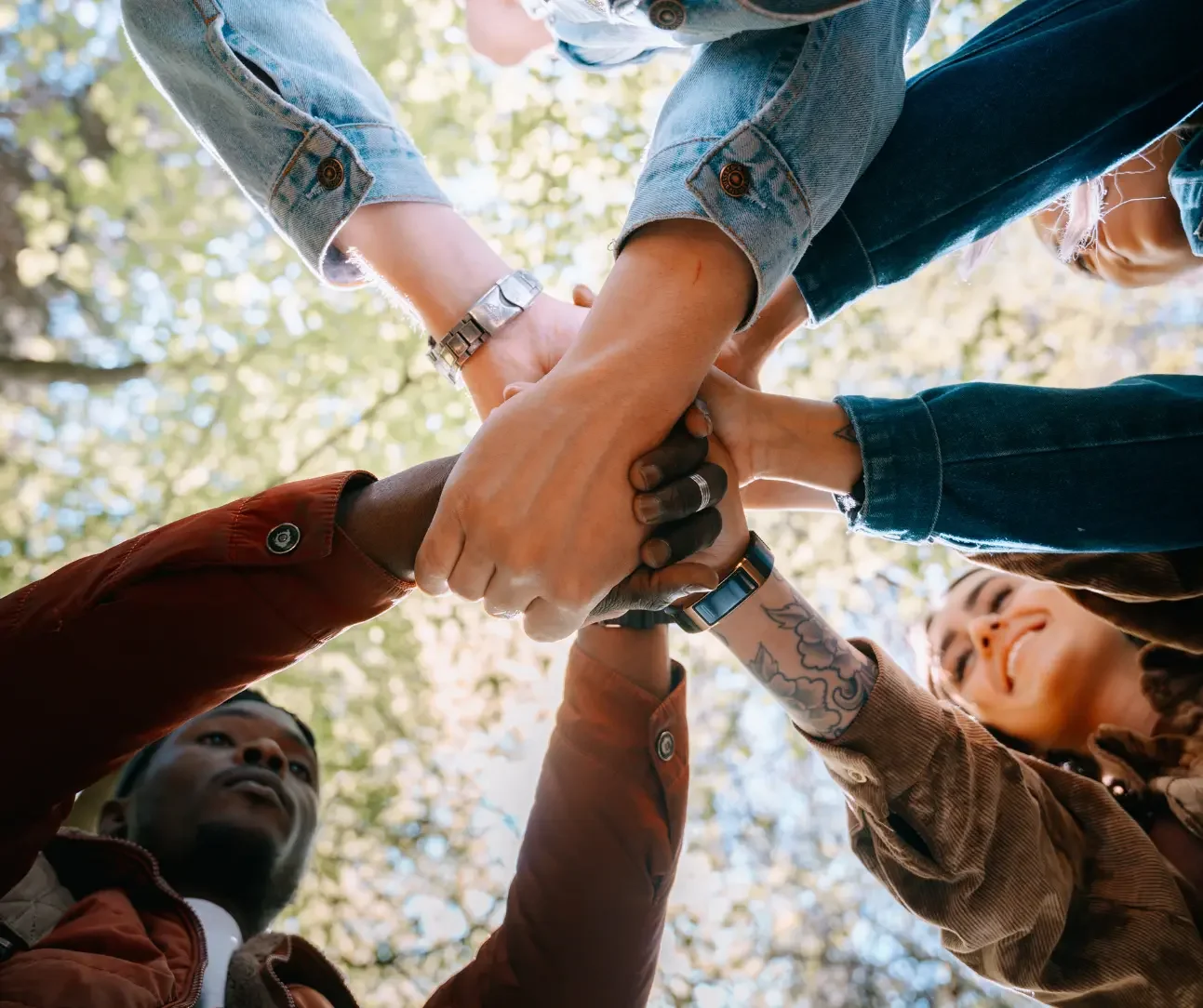 Group of diverse individuals placing their hands together to represent collaboration, support, and community-centered healthcare at True Health Integrative Clinic.