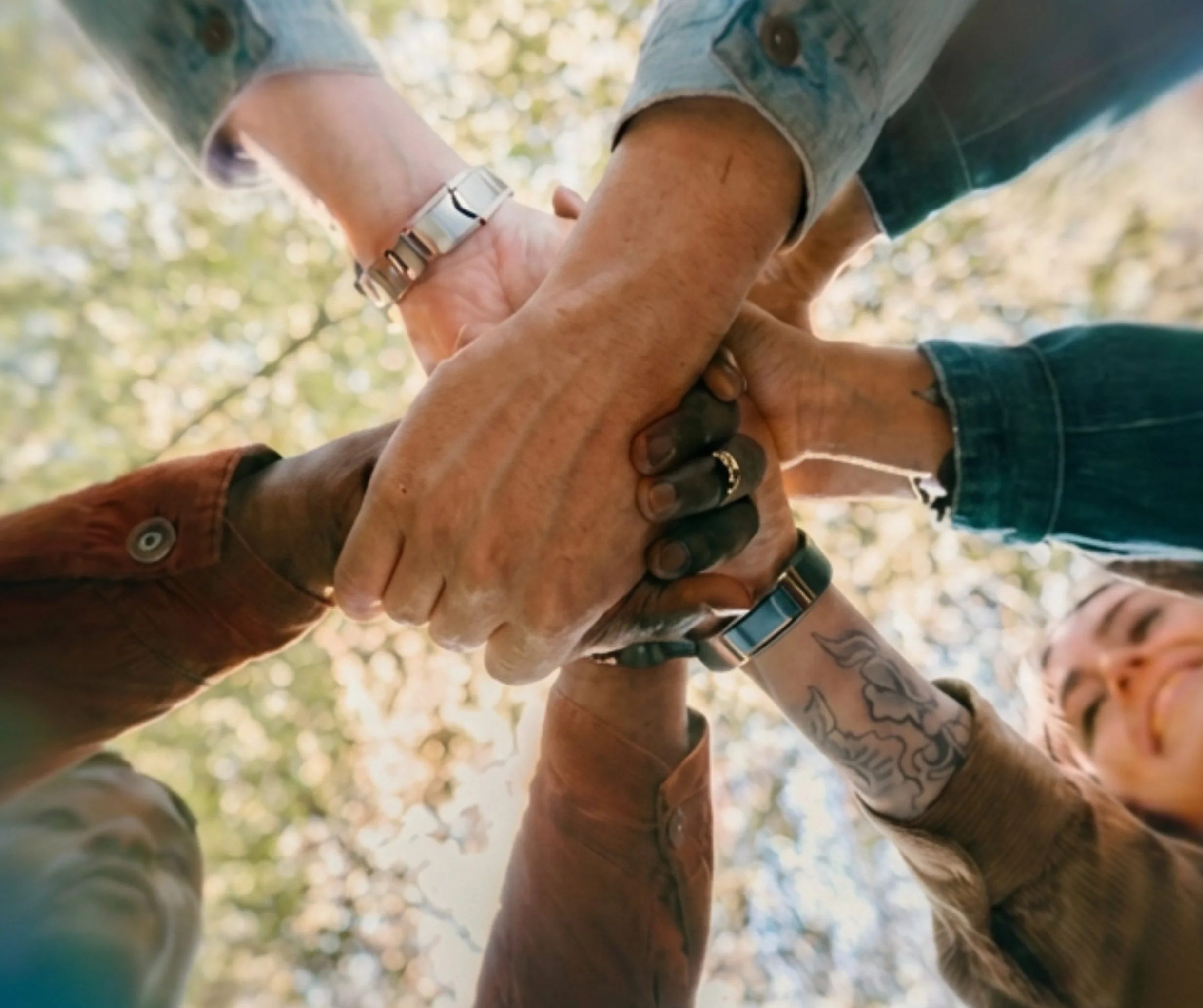 Group of diverse individuals placing their hands together to represent collaboration, support, and community-centered healthcare at True Health Integrative Clinic.