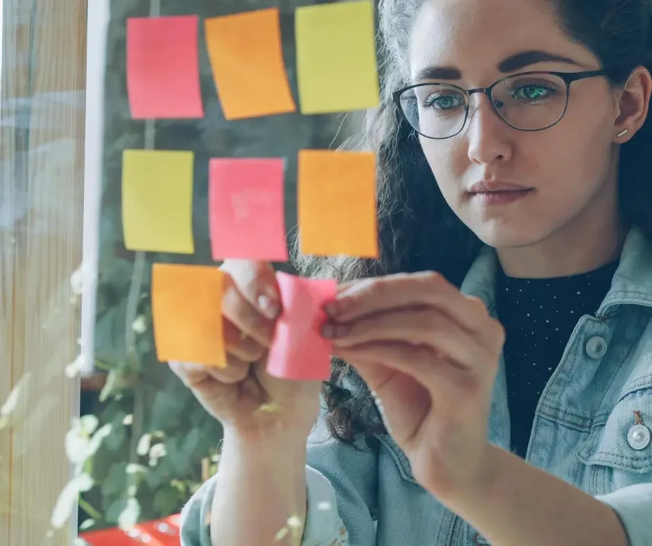 Person organizing notes on a glass wall, representing occupational therapy strategies for executive functioning, organization, and daily life skills.