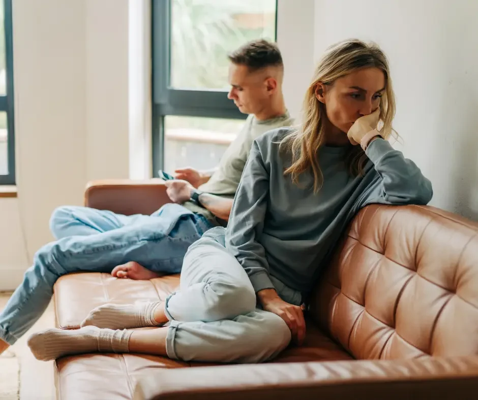 Woman sitting on a couch appearing emotionally distressed, representing the mood and emotional symptoms that can occur with PMS.