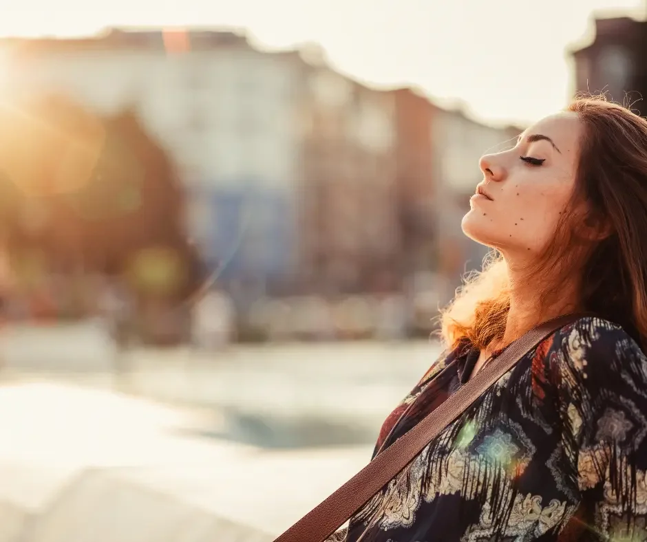 Woman standing outdoors with eyes closed in warm sunlight, representing emotional wellness, stress relief, and mental health support at a therapy and counselling clinic in East St. Paul.