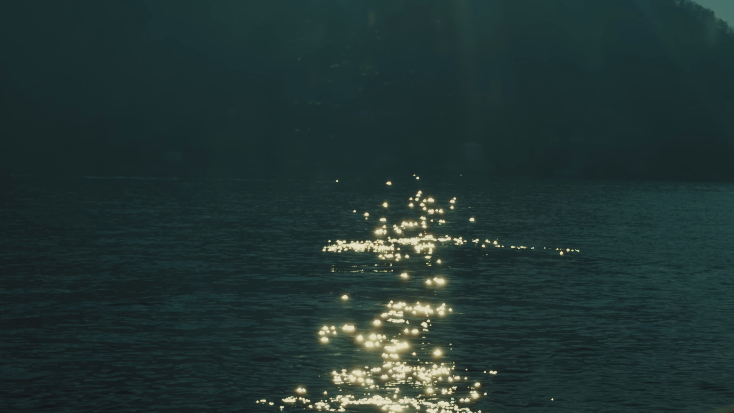 Sunlight reflecting off the surface of a body of water, with dark shoreline or trees in the background.