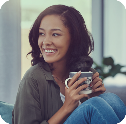 Young woman smiling while holding a mug, sitting on a couch in a bright room.
