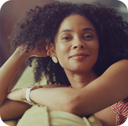 Close-up of a woman with curly hair smiling, resting her head on her arm.