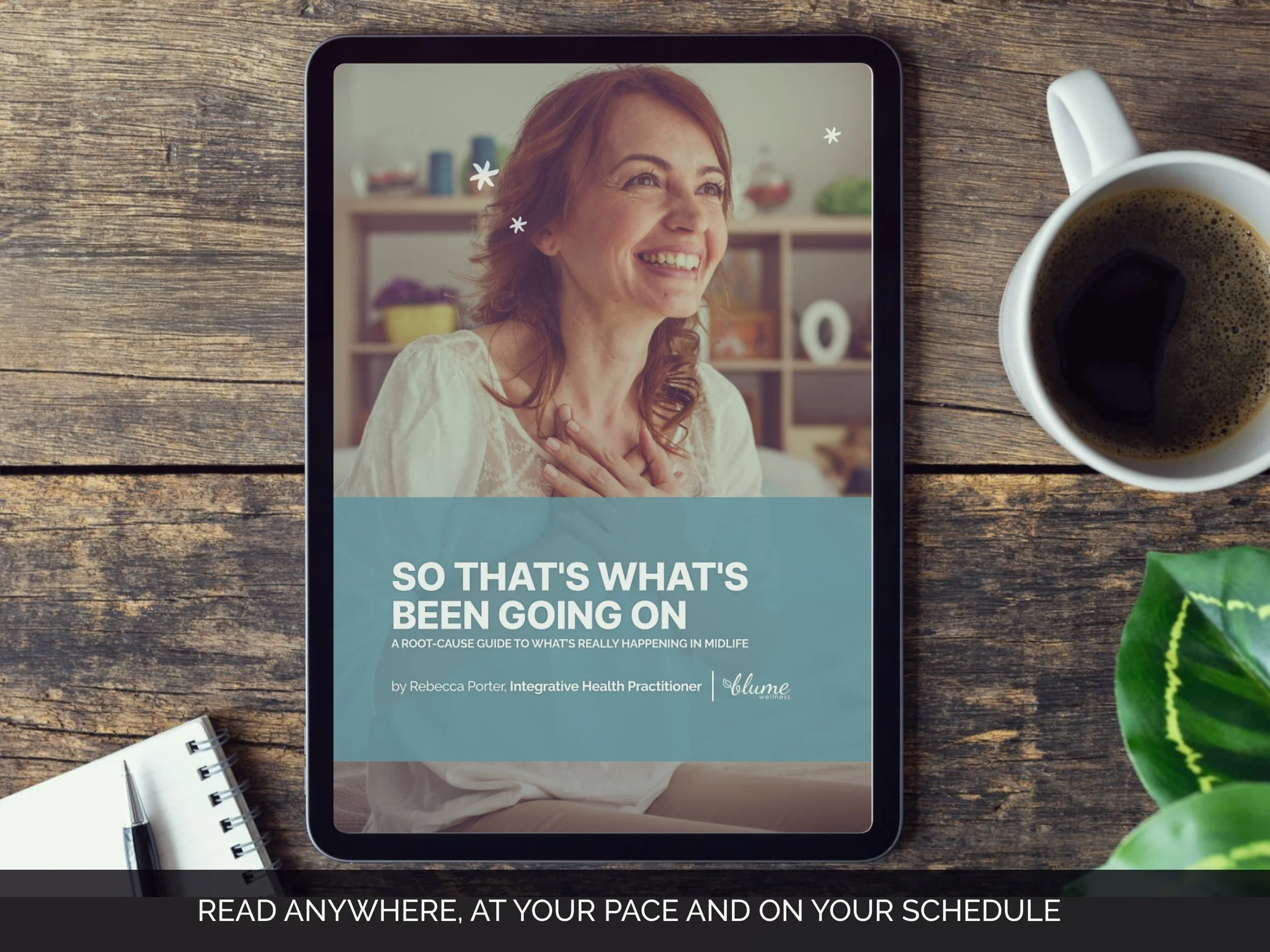 A tablet displaying a woman smiling and touching her chest with text about health and wellness, placed on a wooden table next to a cup of coffee, a spiral notebook, and a pen, with a plant partially visible on the right.