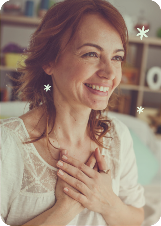 A woman with red hair smiling and holding her hands over her chest.