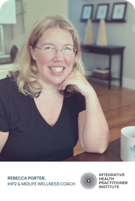 Smiling woman with blonde hair and glasses sitting at a table in a home or office setting, with a mug in front of her and framed pictures on the wall behind.