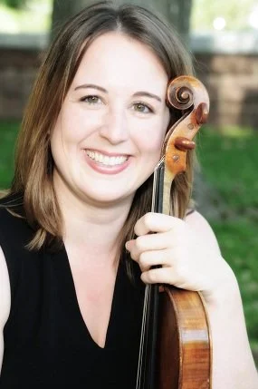 Woman smiling and holding a violin outdoors.