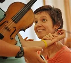 A woman interacts warmly with a person holding a violin, smiling and making eye contact.