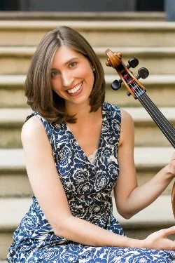 A woman with shoulder-length brown hair smiling and holding a cello.