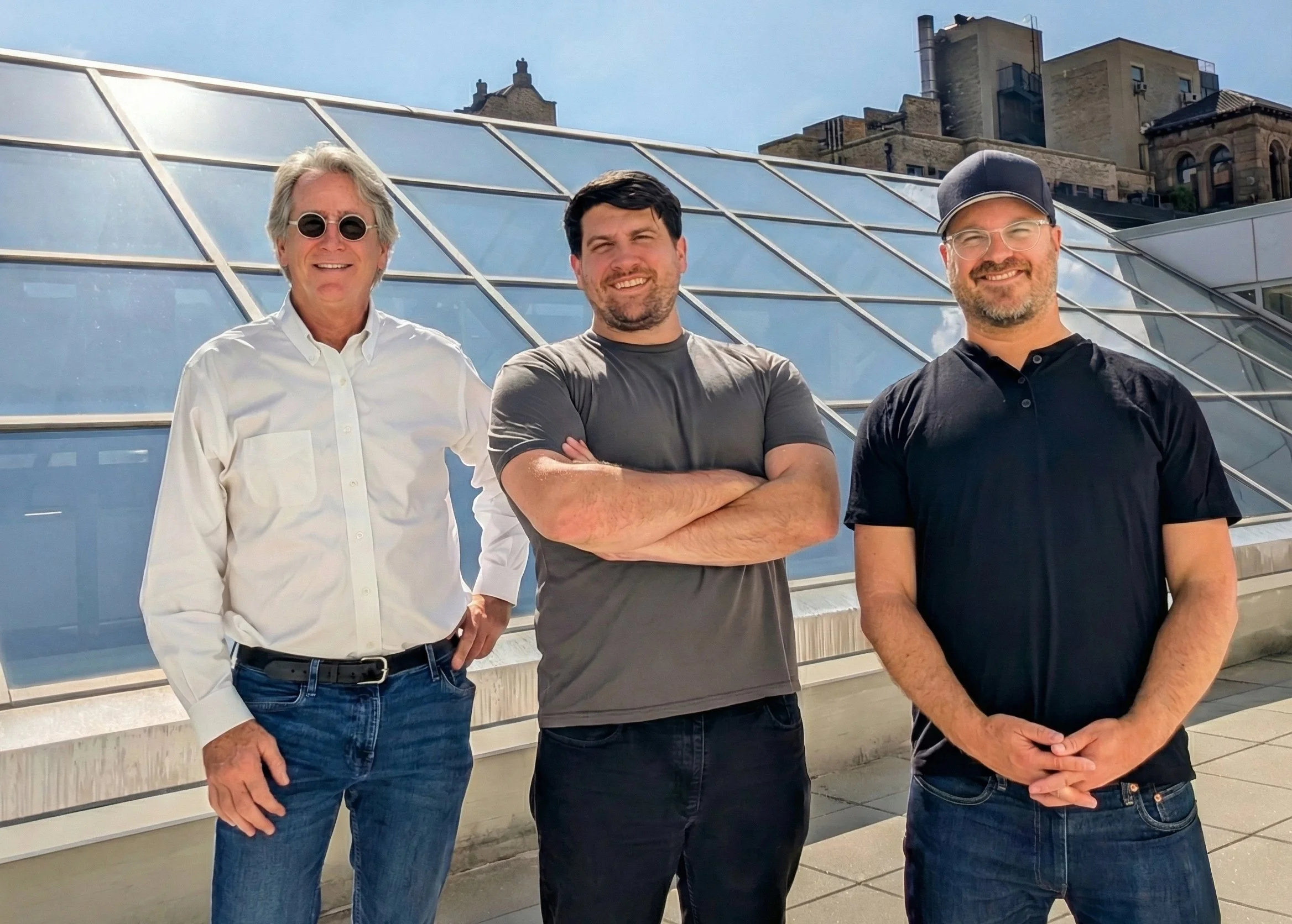 Three men standing outdoors in front of a modern glass building, smiling at the camera.