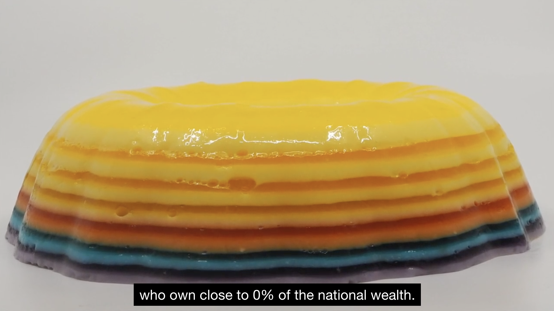 A layered jello mold with stripes of yellow, orange, red, blue, and purple sits on a gray background.