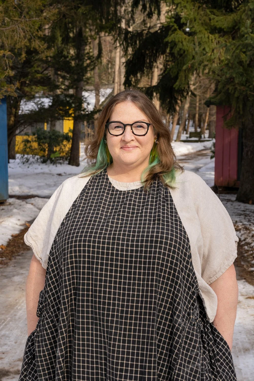 White woman with dark-rimmed glasses and brown hair with bright green streaks standing outside in the snow.