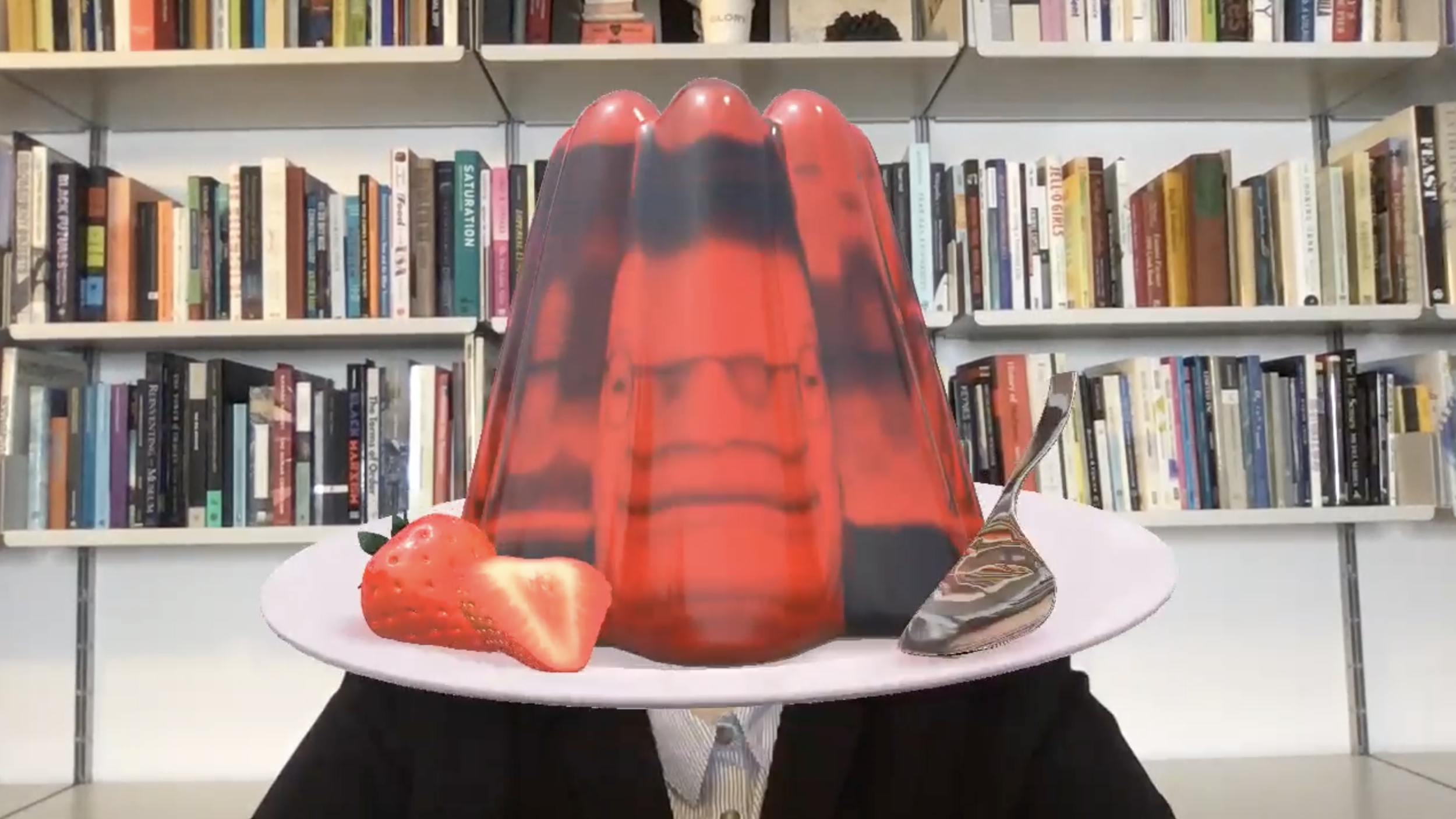 A woman sitting in front of a bookcase with a large red jello mold superimposed over her face.