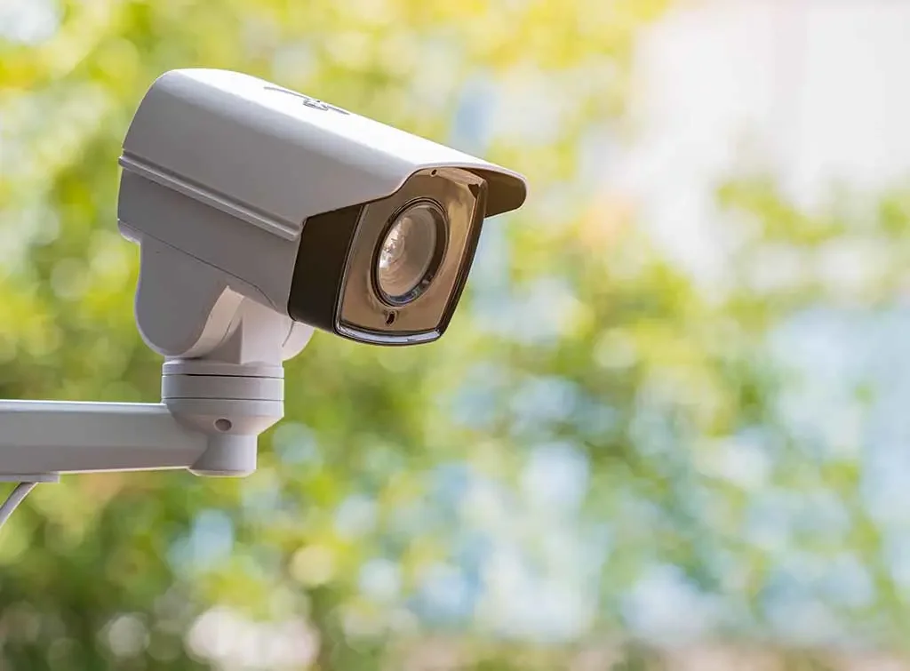 Security camera mounted outdoors with a blurred green and yellow background.