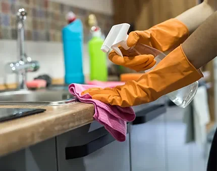 Person wearing orange rubber gloves spraying cleaner on a kitchen countertop.