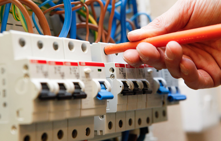 A hand using an orange screwdriver to work on a circuit breaker panel with multiple wires.