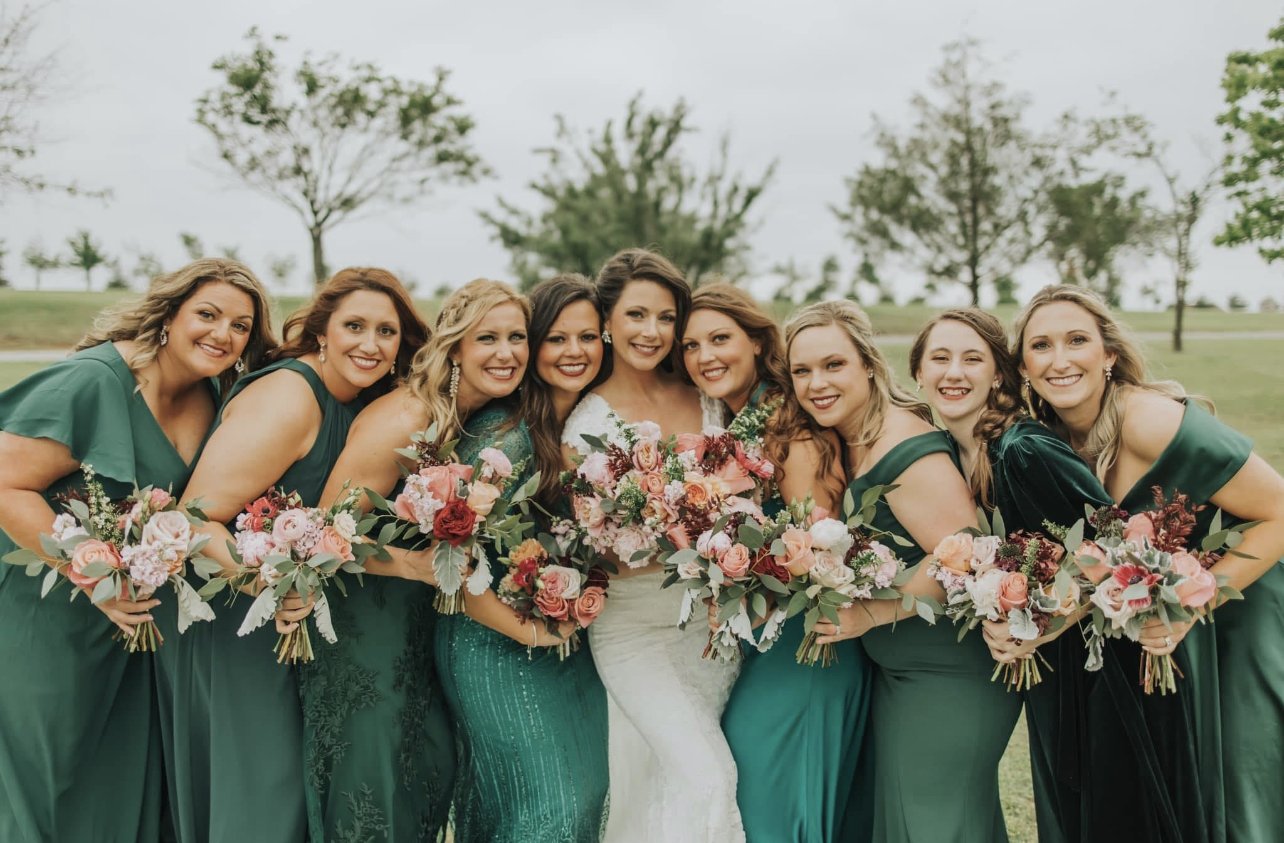 Group of women in green dresses holding bouquets, outdoors on a cloudy day.
