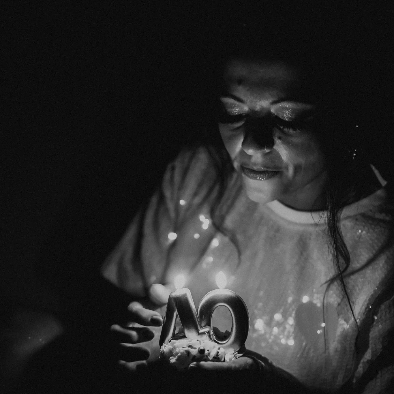 A woman celebrating her 40th birthday with a cake that has a lit candle shaped as the number 40.