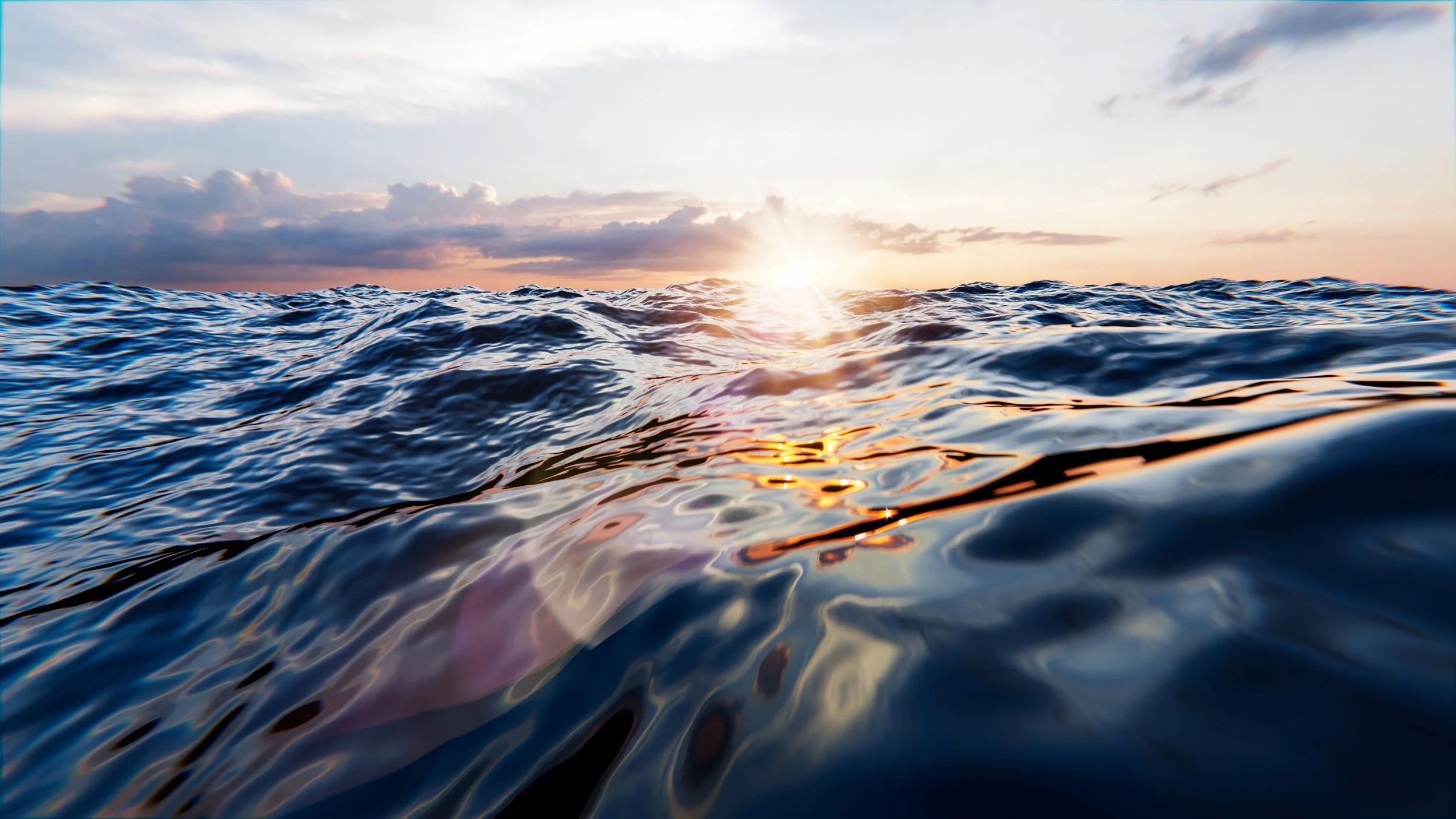 Photo of the ocean waves during sunset or sunrise with the sun on the horizon and clouds in the sky.